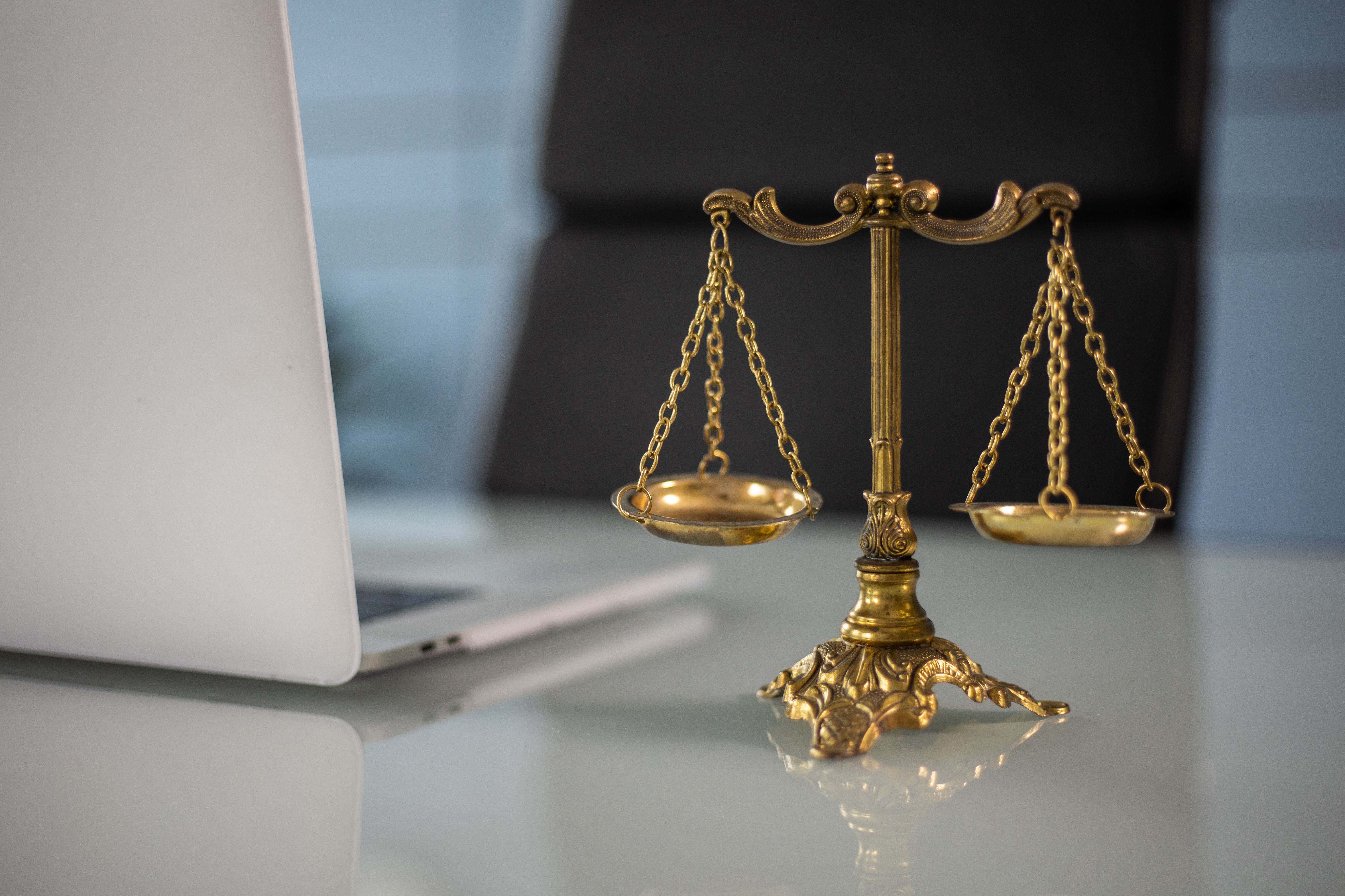 Golden justice scales beside a laptop on a desk, symbolizing law and balance
