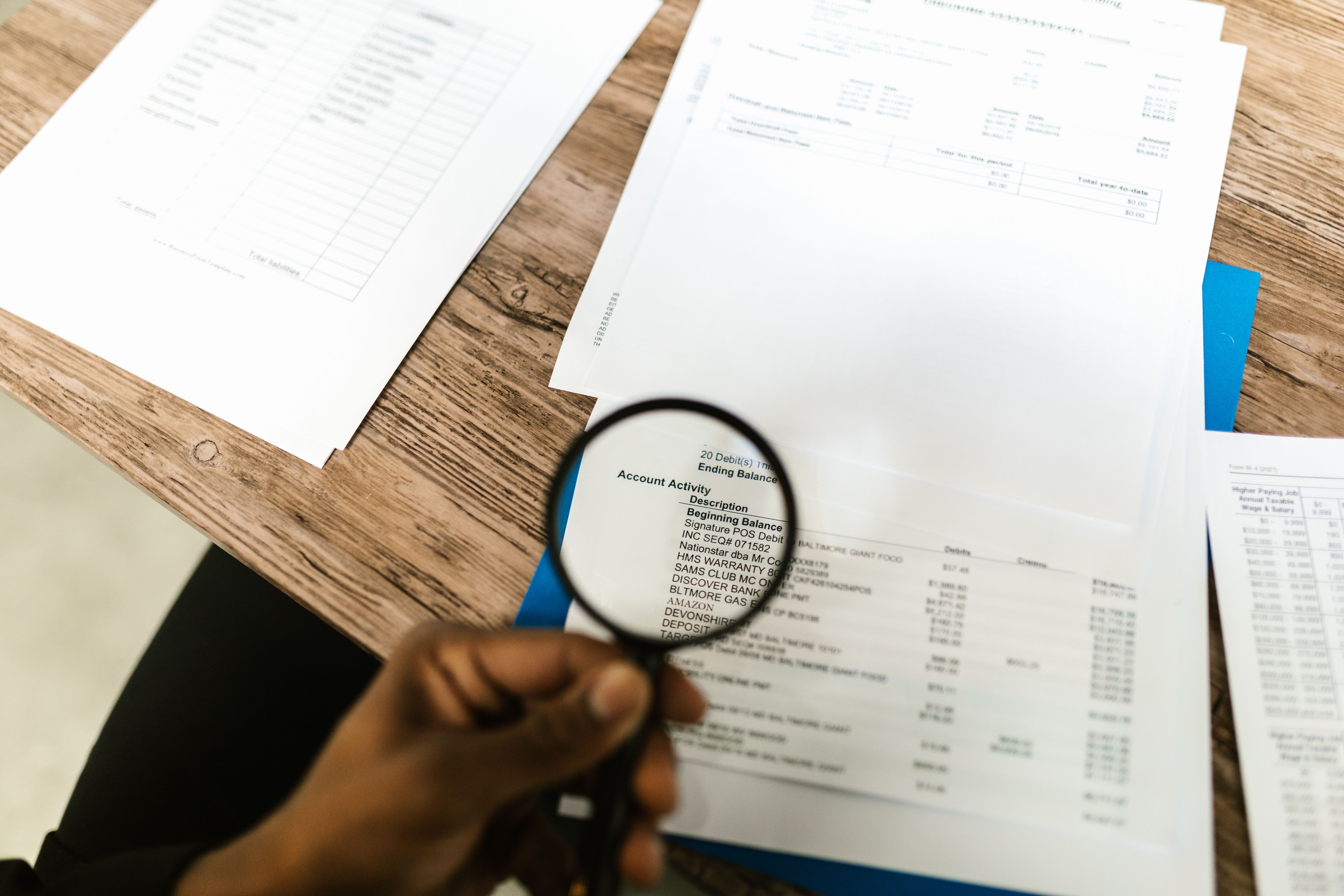 Close-up of hand using magnifying glass to review documents