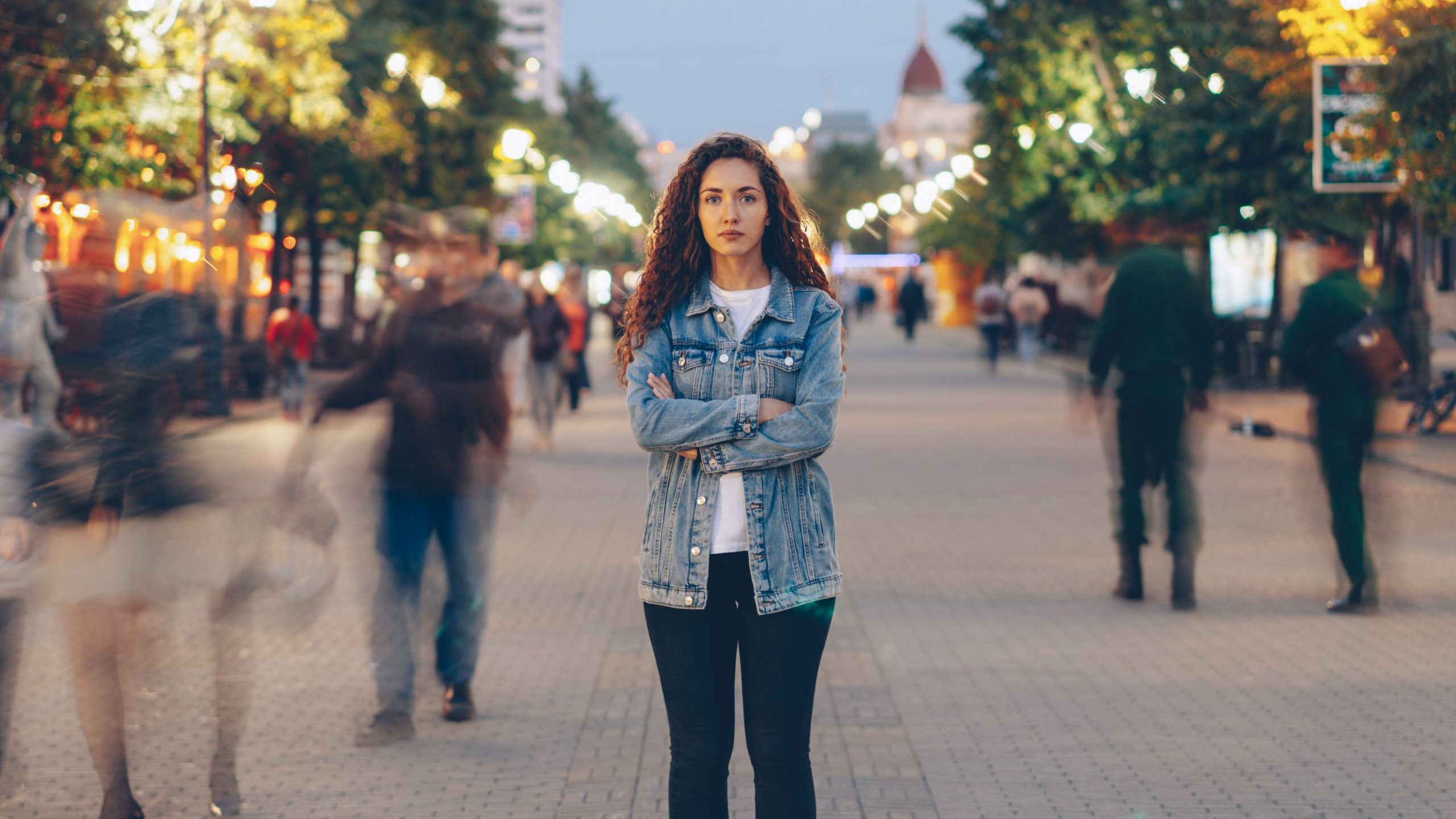 Young woman standing independently on a vibrant city street at dusk